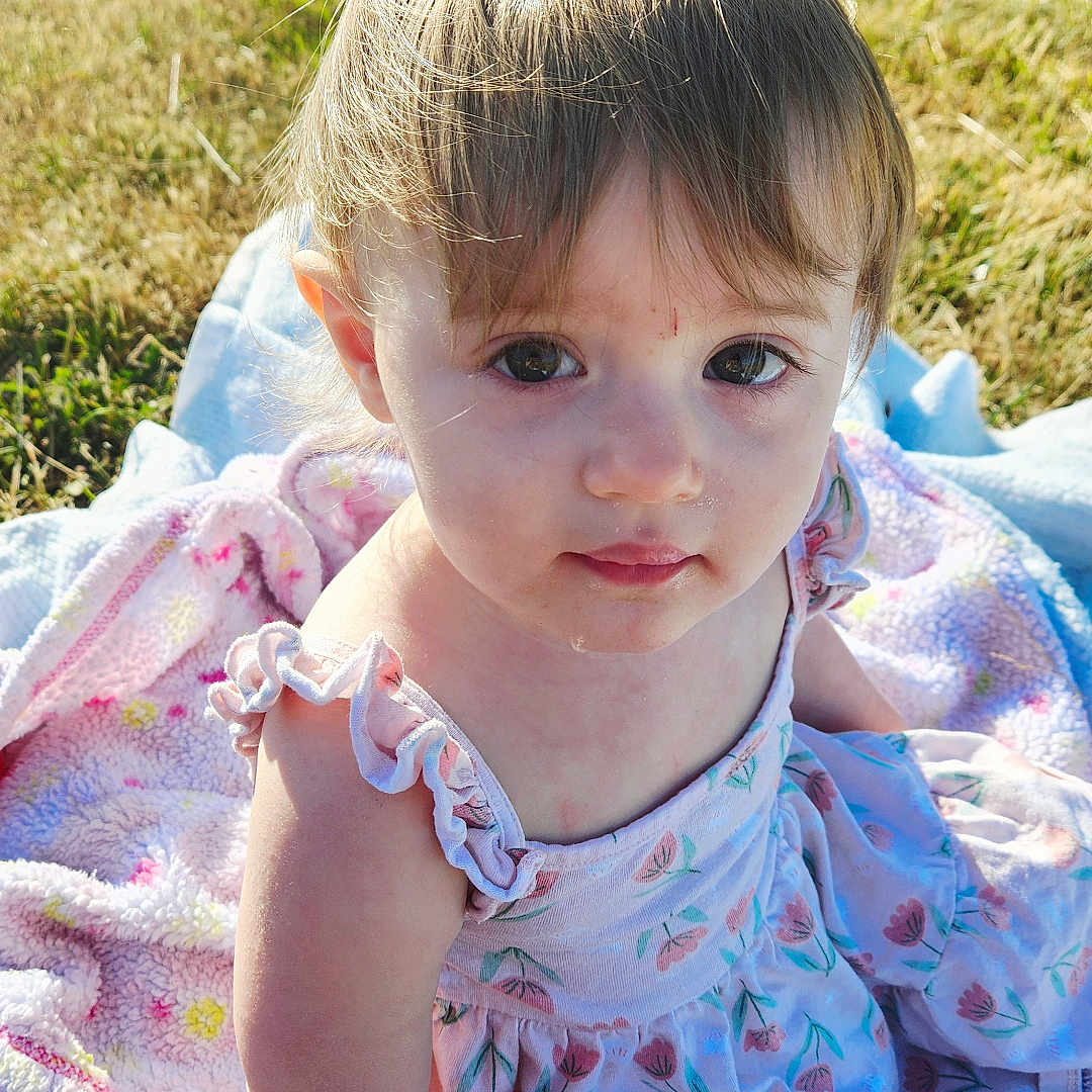 Faylin joined the competition — help win amazing prizes! baby, blanket, child, cute, daylight, dress, eyes, face, floral_pattern, grass, hand, nature, outdoor, play, portrait, sitting, skin, sunlight, toddler, young