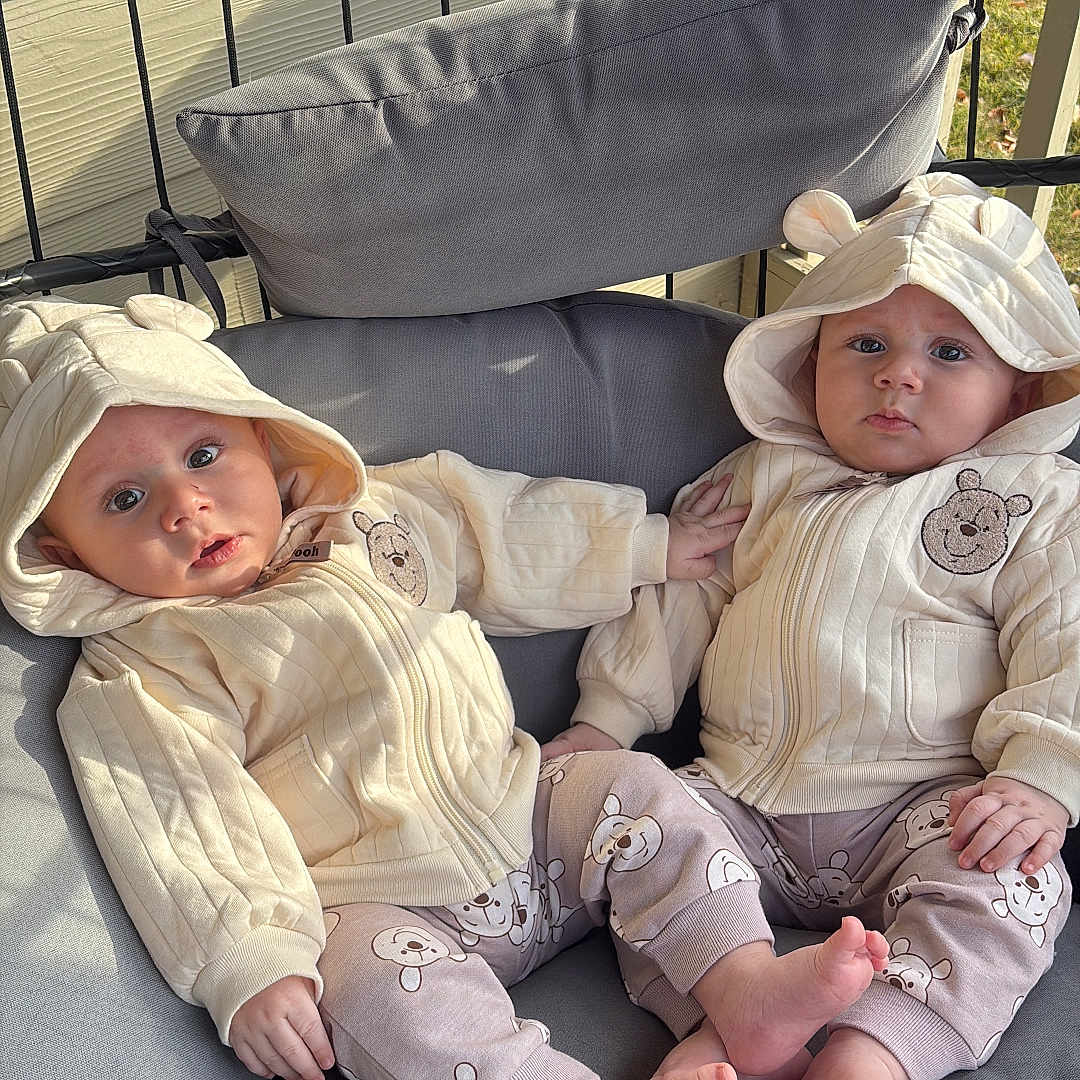 Adam And Yousef joined the competition — help win amazing prizes! baby, bare_feet, bear_ears, bear_print, child, clothing, cushion, cute, expression, face, hoodie, infant, matching_outfits, outdoor, pants, person, porch, seated, swing_chair, toddler