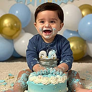 Arjan joined the competition — help win amazing prizes! baby, birthday, cake, blue_cake, balloons, smiling, messy, face_paint, celebration, one_year_old, happy, indoors, carpet, child, sitting, clothing, party, frosting, cute, penguin_sweater