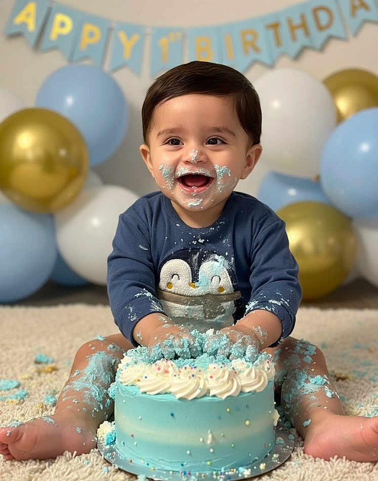 Arjan joined the competition — help win amazing prizes! baby, birthday, cake, blue_cake, balloons, smiling, messy, face_paint, celebration, one_year_old, happy, indoors, carpet, child, sitting, clothing, party, frosting, cute, penguin_sweater