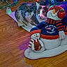cat, christmas_tree, christmas_lights, holiday, festive, snowman, snow_globe, stuffed_toy, plush_toy, apple, football, patriots, scarf, hat, wooden_floor, indoor, pet, animal, colorful_lighting, portrait