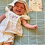baby, infant, smiling, white_clothing, hat, blanket, green, checkered, wooden_sign, flowers, months, cute, happy, lying_down, arm, skin, child, portrait, closeup, adorable