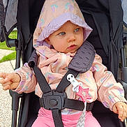 Elena a rejoint le concours — aidez-le/la à gagner de superbes lots ! baby, child, stroller, jacket, hood, pink_pants, safety_harness, clip, star_shaped_toy, outdoor, grass, curious_expression, blue_eyes, hand, seat, canopy, fabric, person, infant, cute