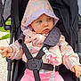 baby, child, stroller, jacket, hood, pink_pants, safety_harness, clip, star_shaped_toy, outdoor, grass, curious_expression, blue_eyes, hand, seat, canopy, fabric, person, infant, cute