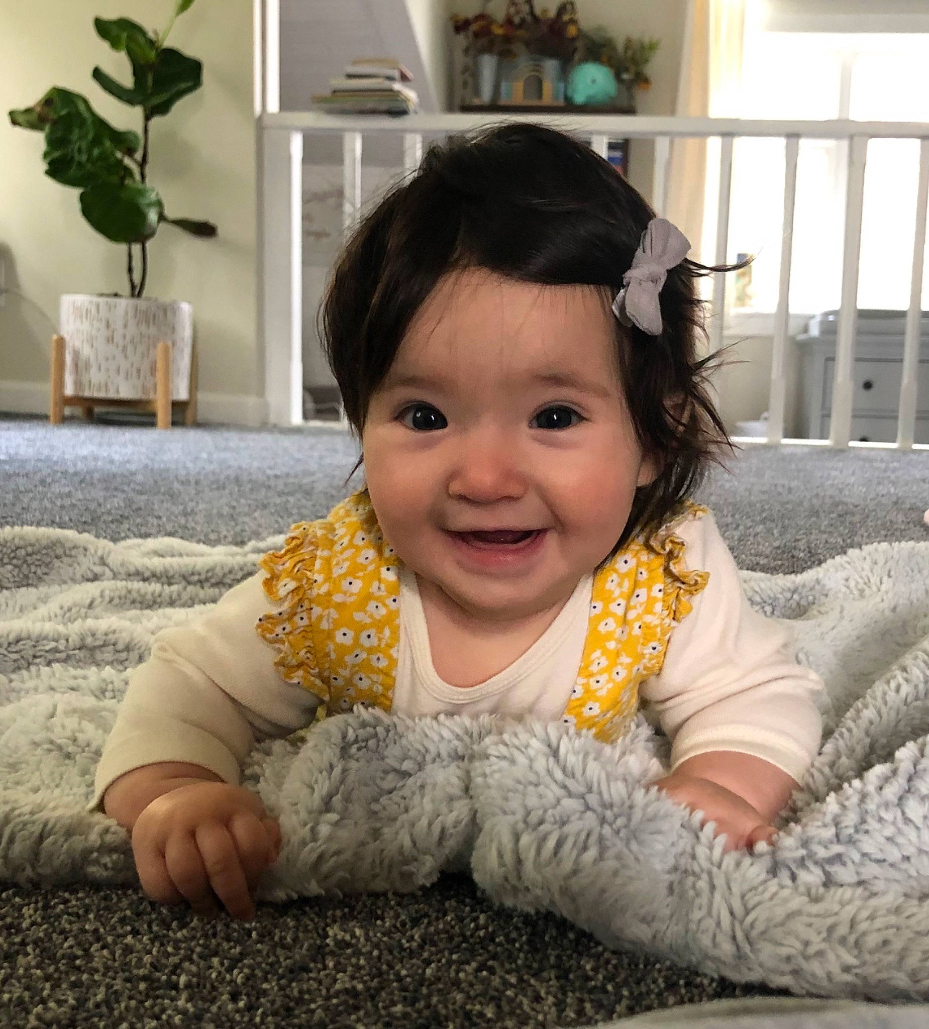 Sienna is registered to the contest to win money with this photo: baby, baby_toddler_clothing, cheek, child, comfort, flooring, flowerpot, fun, gesture, happy, houseplant, joy, linens, person, plant, room, sitting, sleeve, smile, toddler