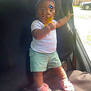 Gabriella joined the competition — help win amazing prizes! toddler, child, car_interior, standing, pacifier, white_shirt, green_shorts, pink_shoes, headband, curly_hair, sunlight, window, seat, seatbelt, playful_filter, whiskers, bow, outdoor_light, vehicle, cute