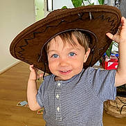 Marceau participe au concours pour gagner de l'argent avec cette photo : toddler, child, hat, cowboy_hat, blue_eyes, striped_shirt, smile, indoor, wooden_floor, cards, plant, basket, face, person, cute, playful, happy, buttoned_shirt, hair, home