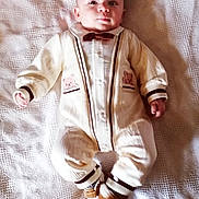 Jules participe au concours pour gagner de l'argent avec cette photo : baby, bear_patch, boots, bow_tie, child, cozy_clothing, cute, expression, face, hands, indoors, infant, knitted_outfit, laying_down, one_person, portrait, socks, soft_lighting, white_blanket, young