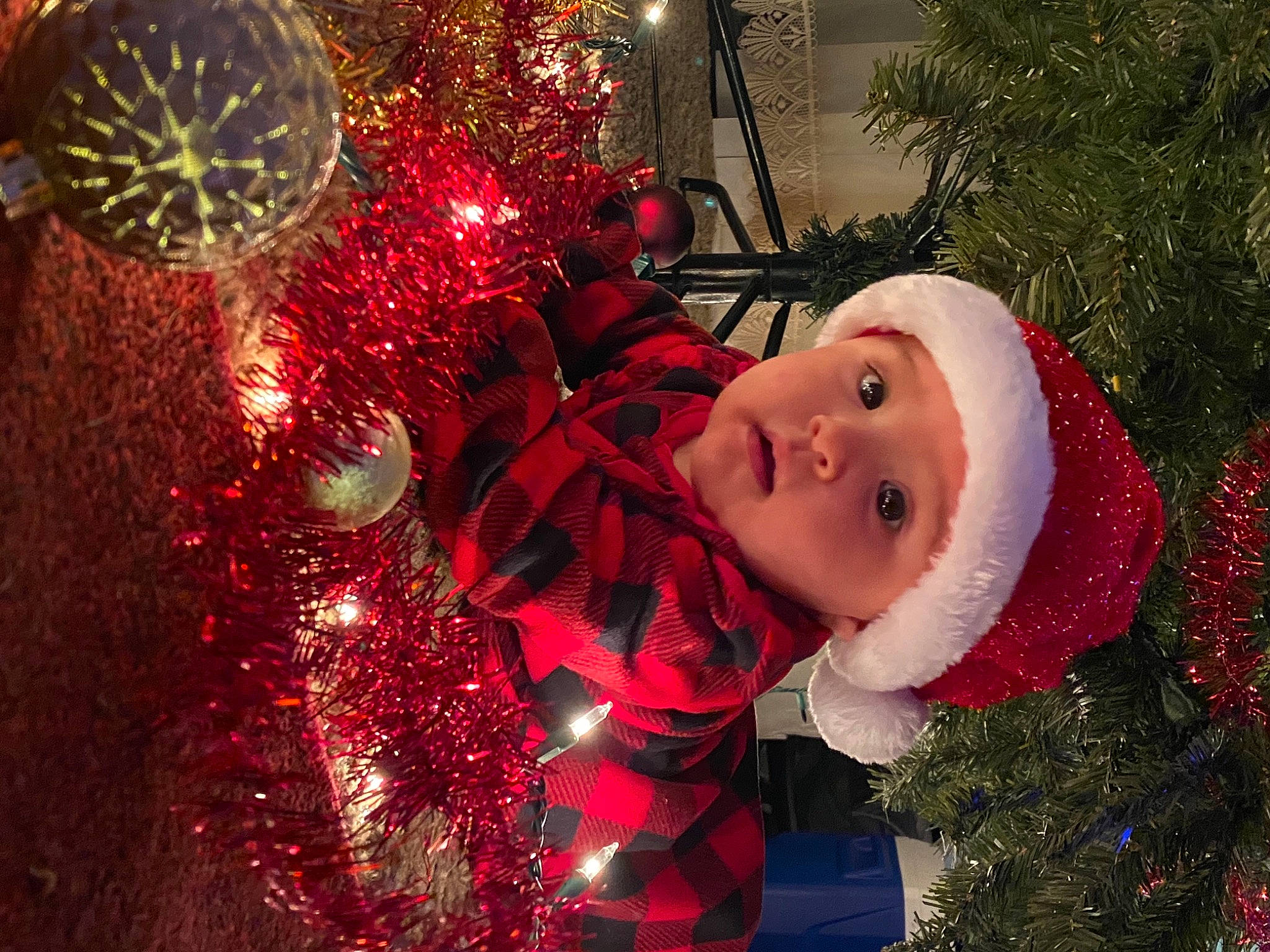 Kamila is registered to the contest to win money with this photo: baby, christmas, christmas_decoration, christmas_eve, christmas_lights, christmas_ornament, christmas_tree, conifer, costume_accessory, event, festival, fictional_character, headwear, holiday, holiday_ornament, interior_design, ornament, person, pine_family, red