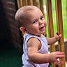 baby, child, smiling, face, person, sleeveless_shirt, wooden_railings, outdoor, green_background, skin, head, arm, portrait, happy, infant, cute, young_child, natural_light, expression, motion