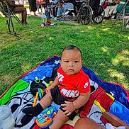 Behr is registered to the contest to win money with this photo: baby, child, person, outdoor, grass, blanket, toy, bottle, scooter, group, wheelchair, balloons, casual_clothing, park, sunlight, people, seated, greenery, shadows, gathering