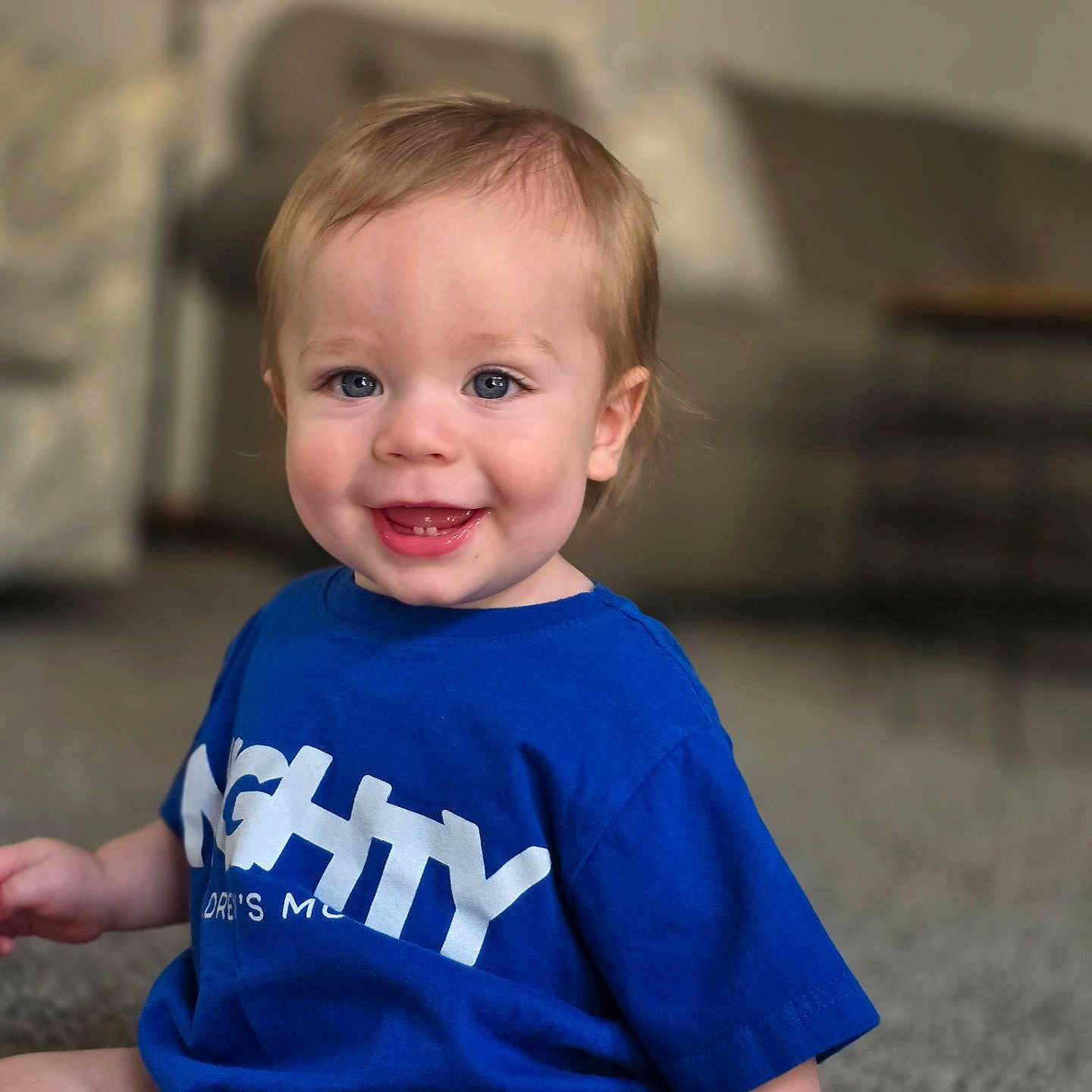 Declan joined the competition — help win amazing prizes! baby, blond_hair, blue_tshirt, carpet, casual_clothing, child, cute, face, happy, home, indoor, living_room, person, playful, portrait, sitting, smiling, teeth, toddler, young_child