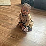 toddler, child, floor, wooden_floor, sitting, indoor, crate, couch, clothing, socks, person, young_child, curious, home, natural_light, flooring, casual, looking, baby, portrait