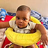 baby, child, infant, yellow_cushion, seat, arm, face, curious, indoor, bed, blanket, stuffed_toy, blue_toy, clothing, person, skin, head, expression, cute, home
