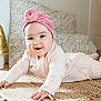 baby, infant, pink_turban, pink_outfit, smiling, lying_down, hands, rug, woven_rug, floor, decorative_lamp, mushroom_lamp, cushion, floral_pattern, indoor, cozy, child, person, cute, happy