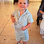 child, clothing, decorations, floor, footwear, happy, home, indoor, nike, person, shirt, shorts, smiling, sneakers, standing, stroller, table, television, toddler, toy