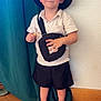 bag, boy, casual_clothing, child, crossbody_bag, curtain, cute, floor, happy, hat, indoors, playful, portrait, red_shoes, shorts, smile, snack, standing, wall, young