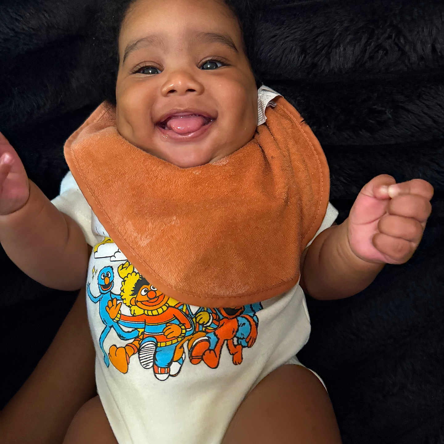 Mazi joined the competition — help win amazing prizes! baby, smiling, tongue_out, bib, onesie, sesame_street, colorful_clothing, happy, infant, cute, child, portrait, indoor, closeup, fuzzy_background, person, skin, hand, face, young