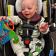 Rivers is registered to the contest to win money with this photo: baby, car_seat, child, toy, mickey_mouse, pajamas, socks, happy, infant, indoor, seatbelt, playful, cute, smiling, childrens_toy, person, clothing, fabric, seat, comfort