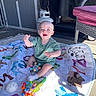 baby, child, smiling, play_mat, toy, outdoor, patio, sunlight, happy, sitting, clothing, sock, colorful, animal_print, plastic_toy, furniture, grill_cover, floor, blanket, person