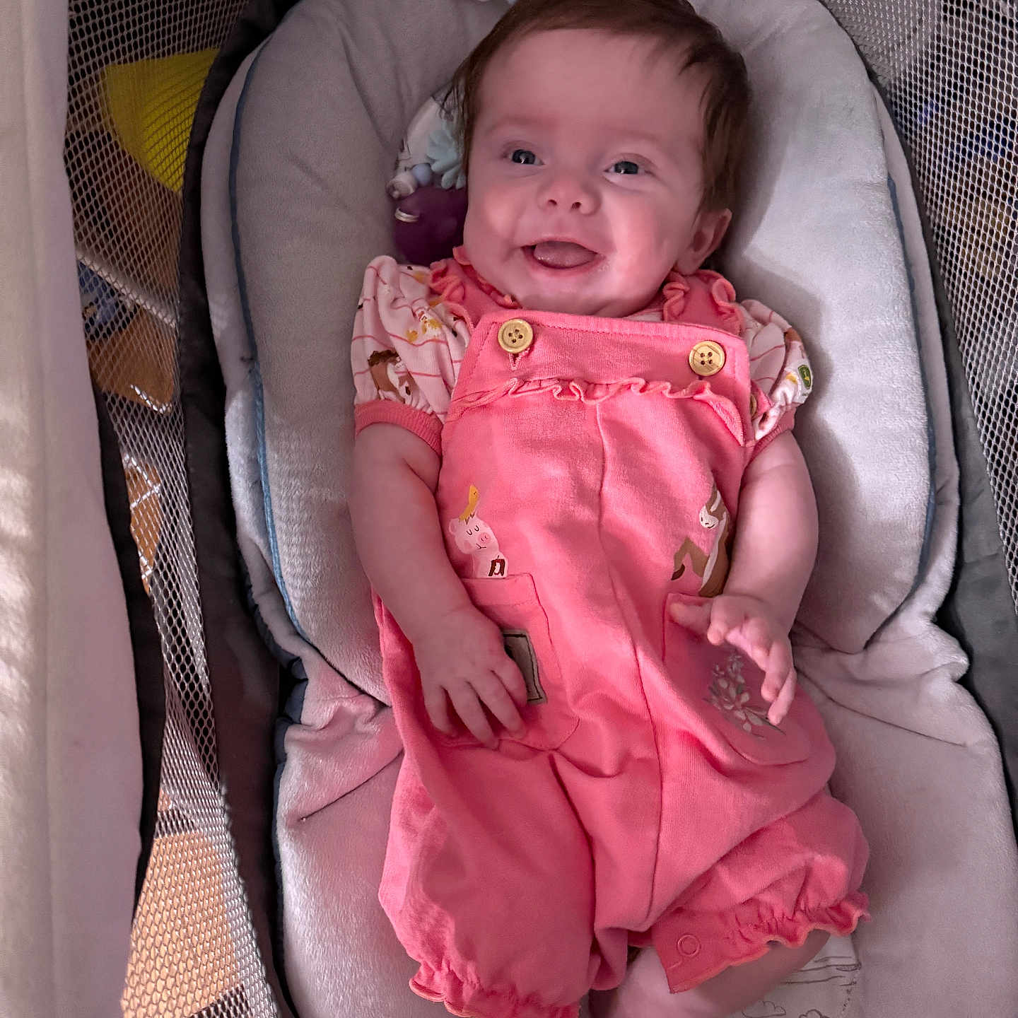 Scarlett is registered to the contest to win money with this photo: baby, baby_seat, child, clothing, cute, face, feet, happy, indoor, infant, legs, mesh_sides, padded_seat, person, pink_romper, playpen, portrait, relaxing, smiling, soft_toys