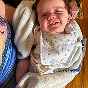 Scarlett joined the competition — help win amazing prizes! baby, smiling, blanket, bib, person, indoor, wooden_floor, clothing, hand, cute, infant, cheeky, holding, closeup, soft_texture, warm_lighting, happy, face, tongue_out, casual