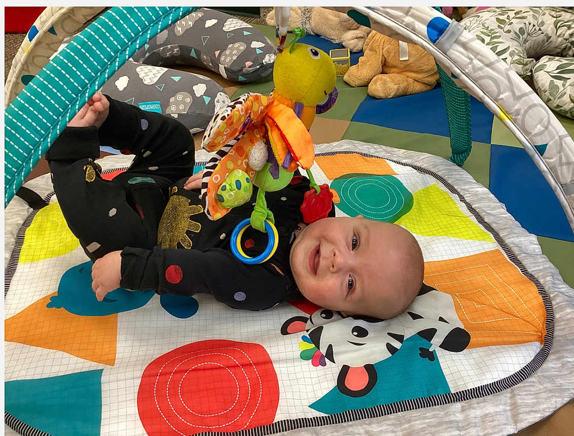 Sebastian joined the competition — help win amazing prizes! baby, infant, play_mat, toy, stuffed_animal, colorful, floor_cushion, child, smiling, indoor, play_area, cute, happy, black_clothing, patterned_clothing, soft_toys, toddler, baby_toy, baby_play, child_playing