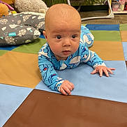 Sebastian joined the competition — help win amazing prizes! baby, infant, tummy_time, blue_onesie, play_mat, colorful, soft_toys, cushions, floor, indoor, child, cute, curious, hands, head, eyes, expression, person, young_child, carpet