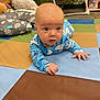 baby, infant, tummy_time, blue_onesie, play_mat, colorful, soft_toys, cushions, floor, indoor, child, cute, curious, hands, head, eyes, expression, person, young_child, carpet