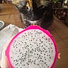 cat, tortoiseshell_cat, dragon_fruit, pitaya, fruit, food, close_up, whiskers, feline, pet, curious, indoor, wooden_table, hand, white_flesh, pink_skin, black_seeds, sniffing, portrait, home