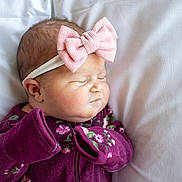 Josie joined the competition — help win amazing prizes! baby, newborn, sleeping, headband, pink_bow, purple_clothing, floral_pattern, infant, soft_pillow, closeup, peaceful, cute, child, portrait, indoor, resting, young_baby, cozy, small_hands, sleep