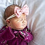 baby, newborn, sleeping, headband, pink_bow, purple_clothing, floral_pattern, infant, soft_pillow, closeup, peaceful, cute, child, portrait, indoor, resting, young_baby, cozy, small_hands, sleep