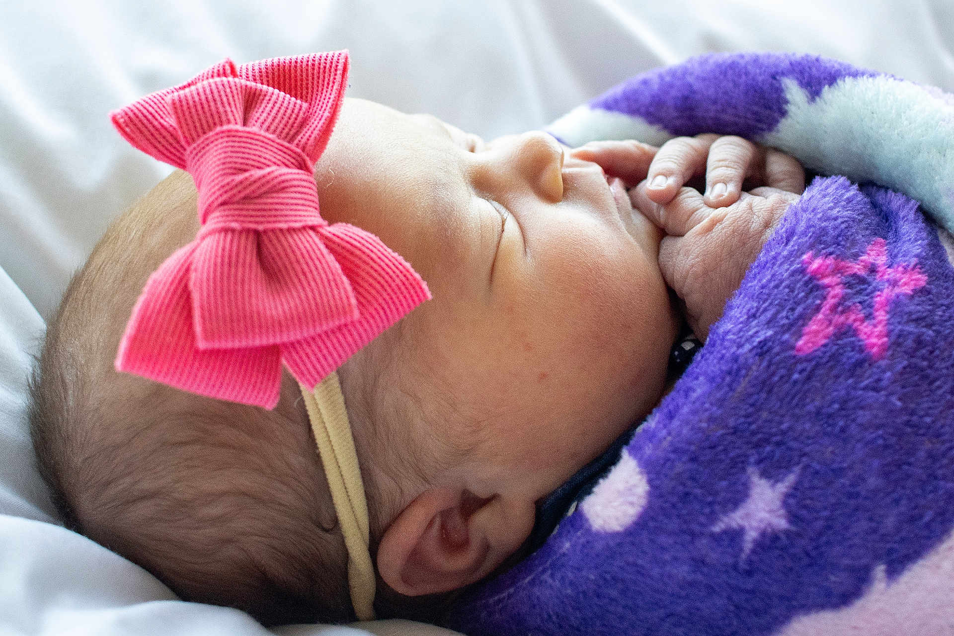 Josie is registered to the contest to win money with this photo: newborn, baby, sleeping, blanket, purple, star_pattern, pink_bow, headband, closeup, face, hand, skin, cute, infant, resting, soft, cozy, child, portrait, peaceful