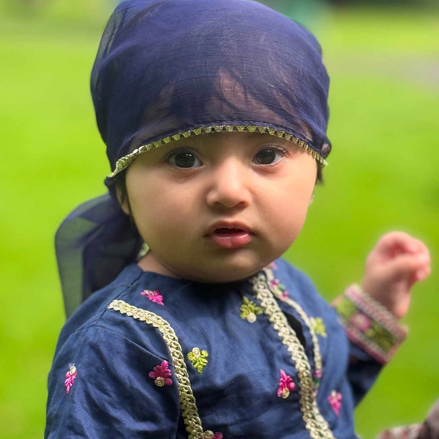 Haya joined the competition — help win amazing prizes! baby, blue_clothing, child, closeup, curious, cute, embroidery, expression, eyes, face, fashion, green_background, headscarf, nature, outdoor, person, portrait, toddler, traditional_clothing, young_child