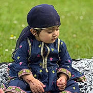 Haya is registered to the contest to win money with this photo: toddler, child, outdoor, grass, blanket, clothing, headscarf, henna, patterned, sitting, cute, portrait, young_child, embroidery, barefoot, nature, person, traditional_clothing, daylight, greenery