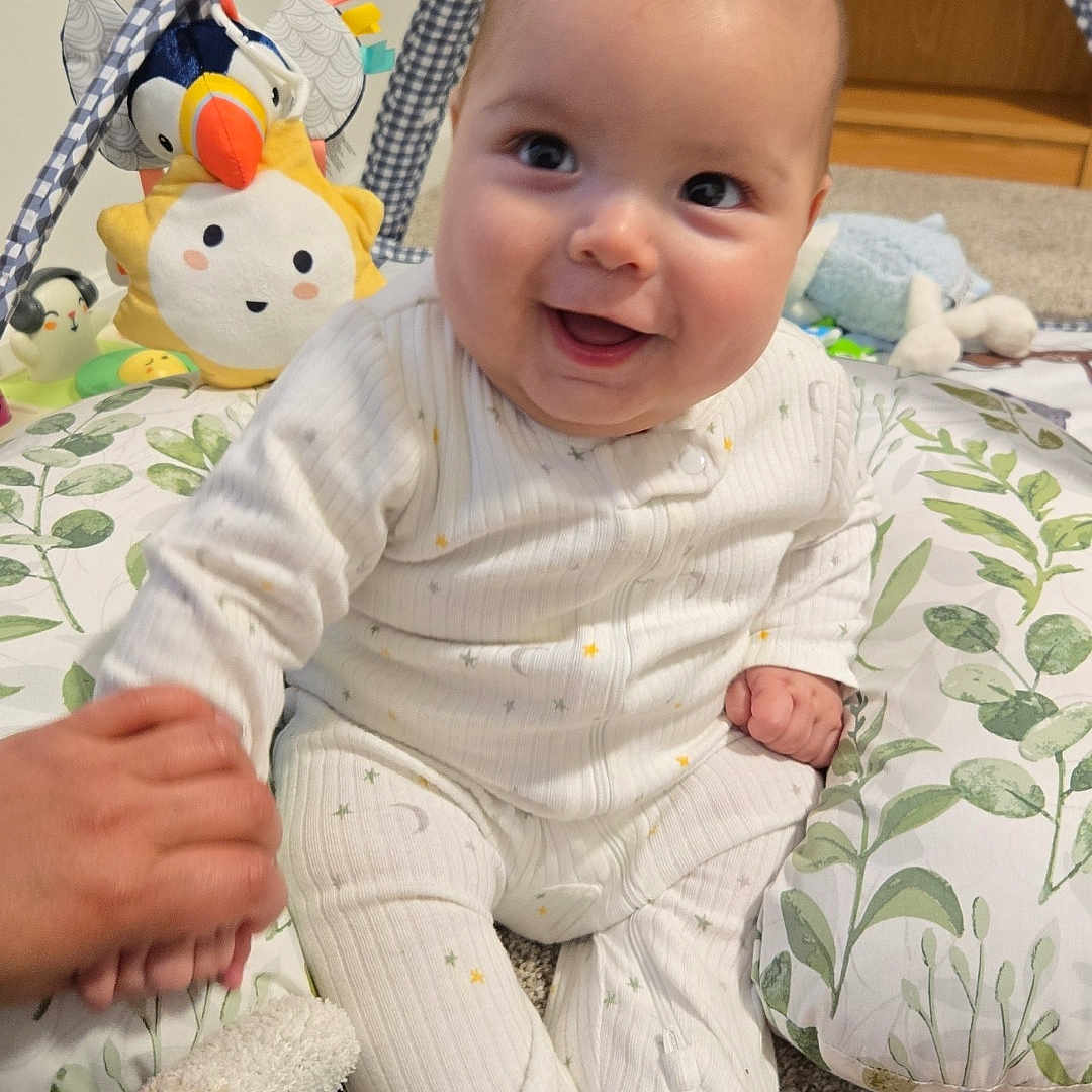 Carson is registered to the contest to win money with this photo: baby, bed, bodypart, clothing, couch, cushion, face, furniture, happy, head, homedecor, hosiery, indoors, pants, person, photography, plush, portrait, sock, toy