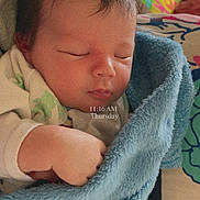 Briere is registered to the contest to win money with this photo: newborn, baby, sleeping, blanket, blue_blanket, infant, wrapped, hand, face, closed_eyes, cozy, soft_texture, indoors, colorful_background, patterned_surface, peaceful, resting, child, person, portrait