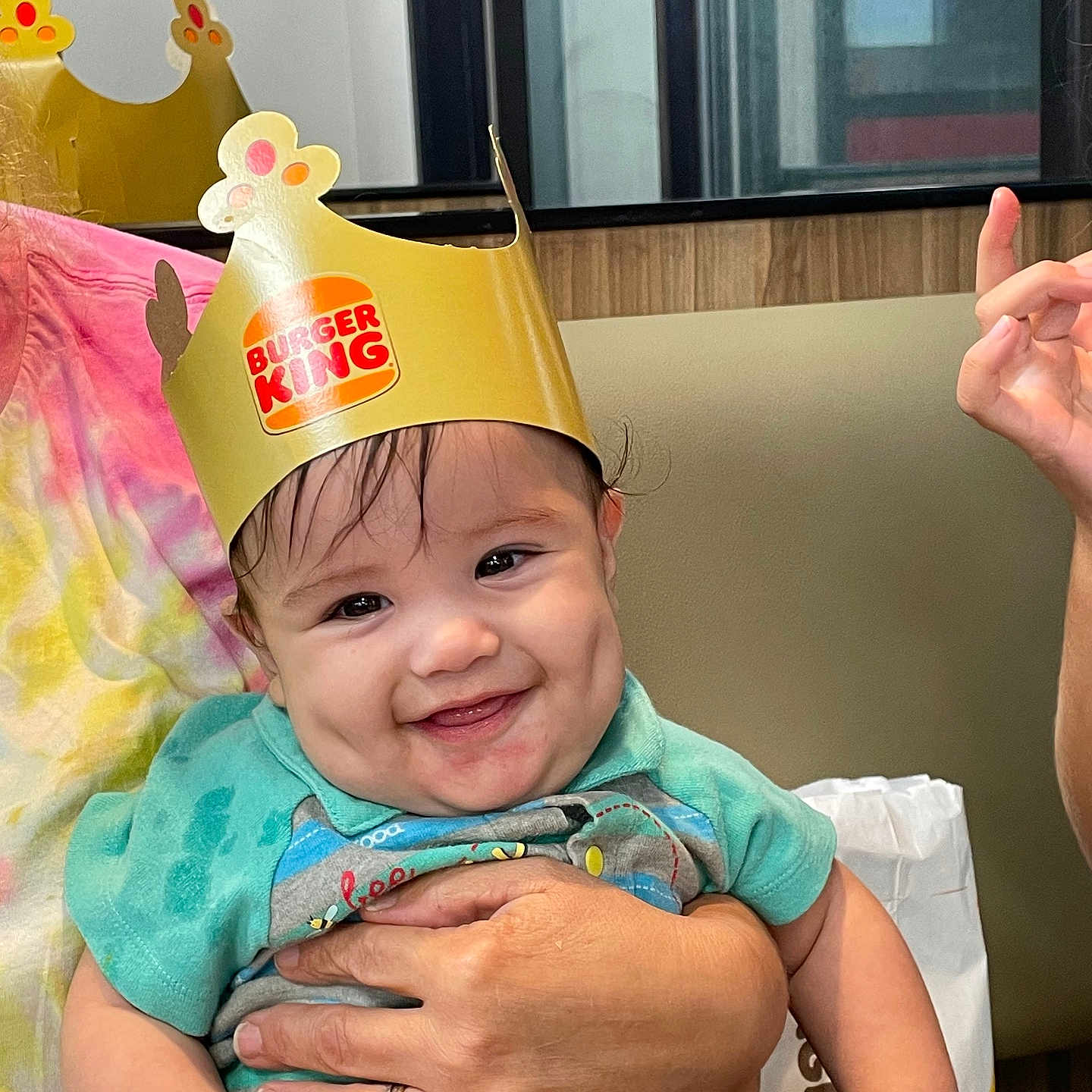 Briere joined the competition — help win amazing prizes! baby, child, smiling, burger_king_crown, burger_king_bag, hand, person, dining_table, tie_dye_shirt, dimples, indoor, seated, happy, cute, portrait, fast_food, restaurant, holding, apparel, headwear