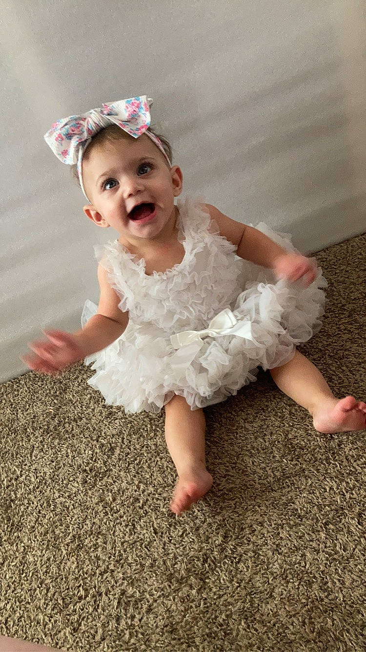 Arielle is registered to the contest to win money with this photo: baby_toddler_clothing, bridal_accessory, child, day_dress, dress, embellishment, fashion_accessory, flash_photography, flooring, hair_accessory, happy, headpiece, human_body, human_leg, person, pink, ruffle, skin, sleeve, smile
