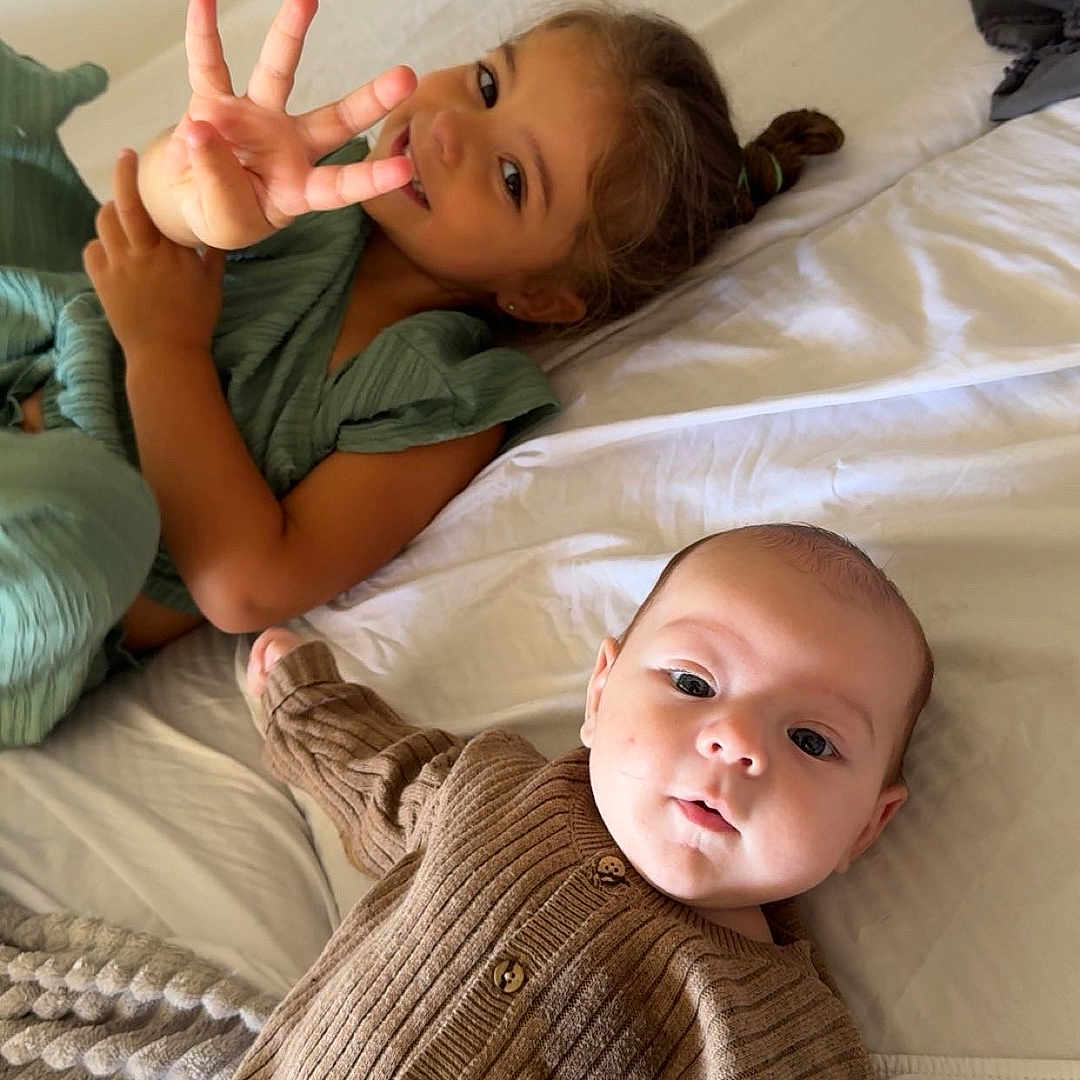 Zayyan a rejoint le concours — aidez-le/la à gagner de superbes lots ! baby, bed, blanket, brown_clothing, child, curly_hair, cute, expression, face, finger_gesture, girl, infant, knitwear, laying_down, light_skin, looking_at_camera, person, playful, smiling, soft_lighting