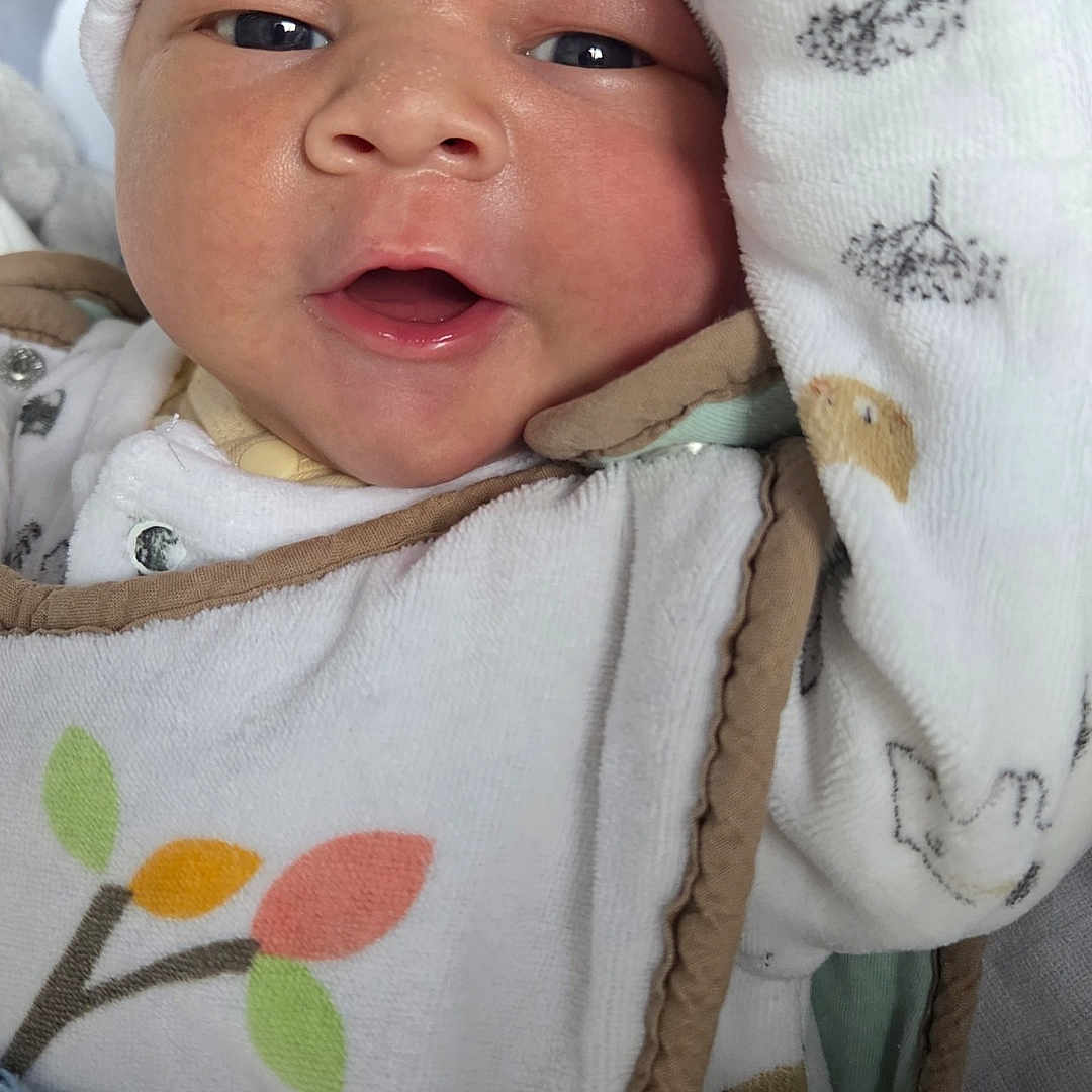 Liam participe au concours pour gagner de l'argent avec cette photo : baby, infant, close_up, white_hat, blanket, cozy, cute, newborn, face, expression, clothing, pattern, leaf, soft, warm, portrait, child, indoors, wrapped, sleepwear