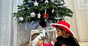 Augustin participe au concours pour gagner de l'argent avec cette photo : baby, boy, child, christmas_tree, curtains, festive, floor, gift_box, headband, holiday_decorations, indoor, interaction, ornaments, pillow, red_dress, santa_hat, smiling, sweater, tiles, toddler