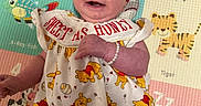 Sadie is registered to the contest to win money with this photo: animal_print, baby, bracelet, child, clothing, colorful, cute, dress, happy, headband, indoors, infant, lying_down, play_mat, portrait, red_bow, smile, smiling, toddler, winnie_the_pooh