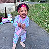 child, toddler, smiling, happy, outdoors, portrait, curly_hair, headband, pink_clothing, pajamas, boots, purse, toy, unicorn_toy, brick_house, yard, grass, driveway, autumn_leaves, standing