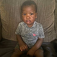 Darren joined the competition — help win amazing prizes! toddler, child, sitting, couch, brown_couch, grey_tshirt, shorts, socks, indoor, portrait, expression, curious, hands, legs, person, young_child, casual_clothing, home, furniture, face