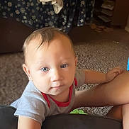 Zayne is registered to the contest to win money with this photo: toddler, child, indoor, living_room, couch, blanket, clothing, carpet, face, blue_eyes, short_hair, furniture, person, curious, reaching, casual_clothing, home, soft_light, baby, expression