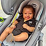 Adriel is registered to the contest to win money with this photo: baby, car_seat, smiling, black_clothing, footwear, jewelry, gold_necklace, child, infant, cute, happy, indoor, seat, fabric, palm_tree, modern, comfortable, person, closeup, portrait