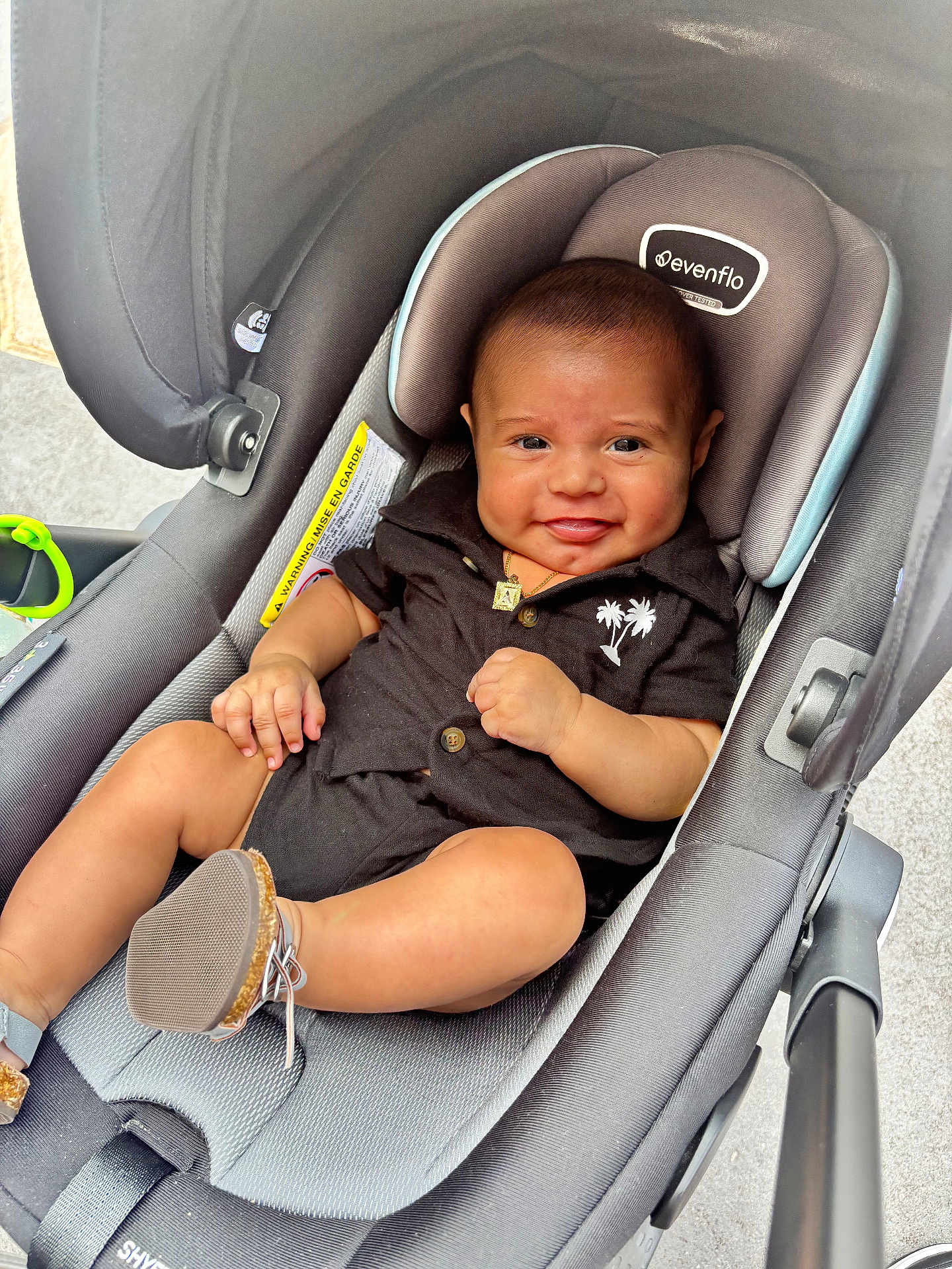 Adriel is registered to the contest to win money with this photo: baby, car_seat, smiling, black_clothing, footwear, jewelry, gold_necklace, child, infant, cute, happy, indoor, seat, fabric, palm_tree, modern, comfortable, person, closeup, portrait