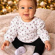 Ambre a rejoint le concours — aidez-le/la à gagner de superbes lots ! baby, child, smiling, blue_eyes, sitting, cozy, blanket, floral_clothing, black_pants, white_socks, indoors, holiday_lights, christmas_tree, festive, cute, portrait, happy, soft_texture, warm_lighting, infant