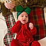 baby, infant, red_clothing, green_bow, headband, plaid_stockings, holiday_decorations, christmas, festive, cute, smiling, indoors, cozy, soft_texture, blanket, child, portrait, happy, celebration, seasonal